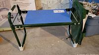Side view showing green metal frame, blue plastic seat, and protective white caps on the legs