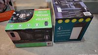 Photo showing the boxed set of 15 solar string lights and 4 solar post accent lights side by side on the floor, with product branding visible.