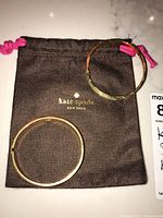 Two gold-tone hoop earrings on top of a brown Kate Spade pouch with pink drawstrings.
