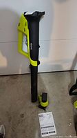 Full view of Ryobi 18V electric leaf blower with battery compartment and instruction manual on concrete floor.