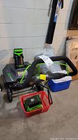 Front and side view of snowblower with handle, wheels, battery and charger placed in front basket