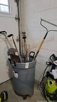 Photo showing several garden tools stored inside a gray plastic pail with wheels.