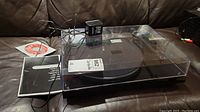 Overall view of turntable on couch with dust cover, power adapter and manuals