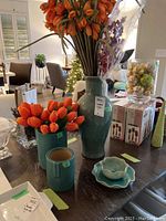 View of two ceramic vases filled with orange faux tulips, small dish set, and other decorative items on table