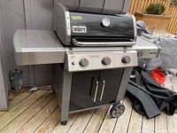Front-left view of grill showing lid, side tables and cabinet base
