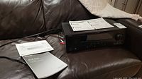 Yamaha AV receiver model HTR-6230 placed on a leather couch with its manuals.