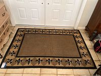 Full view of rectangular area rug with beige background, black and cream Fleur de Lis border design.