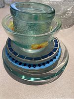 Stack of assorted glass candle holders and holder plates showing textured and smooth surfaces, and a blue mosaic tile plate.