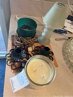 Photo showing all items together: a green candle in metal holder with grape design, large multi-wick candle in clear jar, three black metal candle holders, and a cream-colored ribbed glass holder.