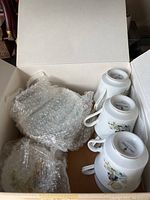 Open box showing 6 Holly Hobbie porcelain cups stacked upside down, wrapped in bubble wrap.