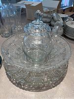 Photo showing the three cut glass items stacked: a large serving plate on the bottom, a smaller plate in the middle, and a covered jar on top, all clear cut glass with intricate designs.