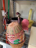 Metal monkey statues, multicolored woven basket in foreground, small pink metal chair, yellow basket in background