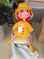 Handmade girl doll in yellow rain gear sitting on a mini wooden chair, showing full body and outfit detail.