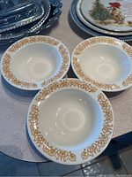 Three white ceramic saucers with ornate gold rim designs