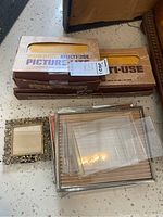 Two cardboard boxes labeled as multi-use Picture Lites next to five picture frames including an ornate small metal frame, a larger silver frame and several others with glass or plastic covers