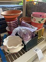 Photo showing assorted ceramic and terracotta planters stacked, some with floral and striped painted designs, white scalloped edge planter, and a black plastic container.