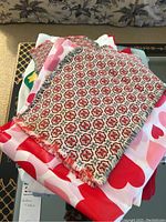 Folded assorted table linens stacked on a black surface showing patterned placemats on top and partial view of other linens below featuring heart prints