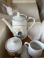 Porcelain teapot with lid and sugar bowl with lid showing Holly Hobbie character and gold rim detailing.