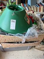 Photo showing green Stand'em Tall Christmas Tree Stand inside a box with Christmas decorations including wreaths.