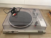 Full view of Technics turntable with plastic dust cover in place, RCA output cables trailing behind.
