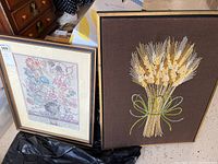 Two framed wall art pieces side by side on floor, tapestry on right and floral print on left