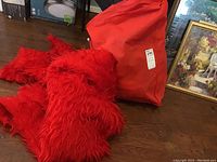 Red furry textured fabric likely part of the Elmo costume seen alongside a large red storage bag.