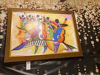 Framed colorful abstract art print showing multiple musical instruments and figures, with a warm brown frame.