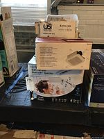 Photo showing three boxed bath fans stacked on a table, including HomeNetWerks, Utilitech, and Broan brands.