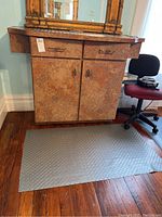 Front view of the salon cabinet showing two drawers and two doors with metal handles and brown mottled finish. Floor mat and part of a chair visible.