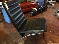 Side view showing the black leather padded seat and backrest with horizontal stitching and curved chrome metal frame supporting the chair.