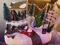 Miniature Christmas decoration scene with flocked pine trees, red truck, and figurines on a snowy base