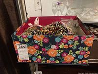 Floral decorated box filled with necklaces, bracelets, and other costume jewelry pieces for children.