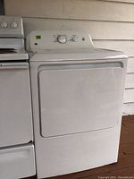 White GE electric dryer with dent on top, front view.