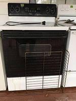 Full front view of the GE electric stove showing the oven door with rack and cooktop surface. White body with some wear and marks visible.