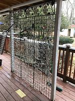 Wide angle photo of four metal display frames with grid design and hooks leaning against a wooden railing outdoors.
