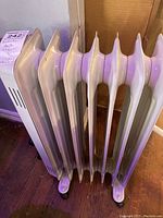 Angle view of the cream-colored oil filled radiator heater showing the vertical fins and wheels.