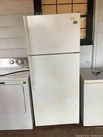 Front view of white Whirlpool top-freezer refrigerator with some dirt marks and two door handles on white exterior.