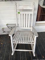 Front view of the white wooden rocking chair showing vertical slat back and slatted seat with some paint chipping.