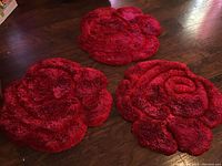 Three round rugs shaped like rose flowers in various shades of red laid on a wooden floor.