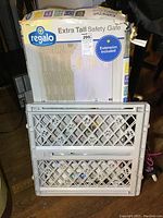 Photo shows boxed extra tall safety gate by Regalo with gate positioned in front of box.