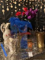 Front view of assorted ceramic and glass vases, pitchers, and faux flowers with blue mesh fabric.