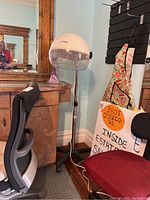Wide view showing the vintage ConairPro standing hair dryer with cream-colored dome hood, office chair, and nearby furniture.