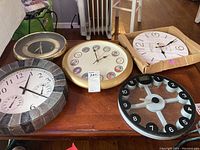 Overview of five wall clocks placed on a wooden table, showing variety of styles and designs.