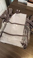 Stack of clear plastic gift bags with brown trim and button handles, arranged on a surface.