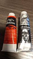 Two tubes of Winsor & Newton Artisan water mixable oil colours: Cadmium Red Medium and Ivory Black.