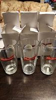 Three Budweiser branded beer glasses standing upright in front of their original white boxes with tops open.