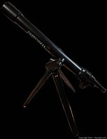Full view of black Bushnell 345 telescope on small tripod against black background.