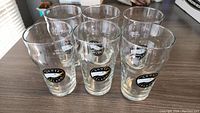 Six Goose Island 20oz beer glasses arranged in a group on a tabletop, showing the logos clearly from the front.