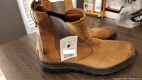 Side view of one tan brown leather boot showing original price tag attached to the back pull tab and rugged outsole.