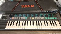 Top view of Yamaha PSS-170 keyboard and Yamaha branded black soft padded carrying case behind it.